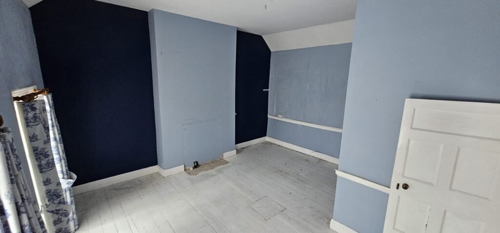 Empty room with pale blue and dark blue walls, white wooden floor, and a white door, possibly in a house being relocated by local movers.