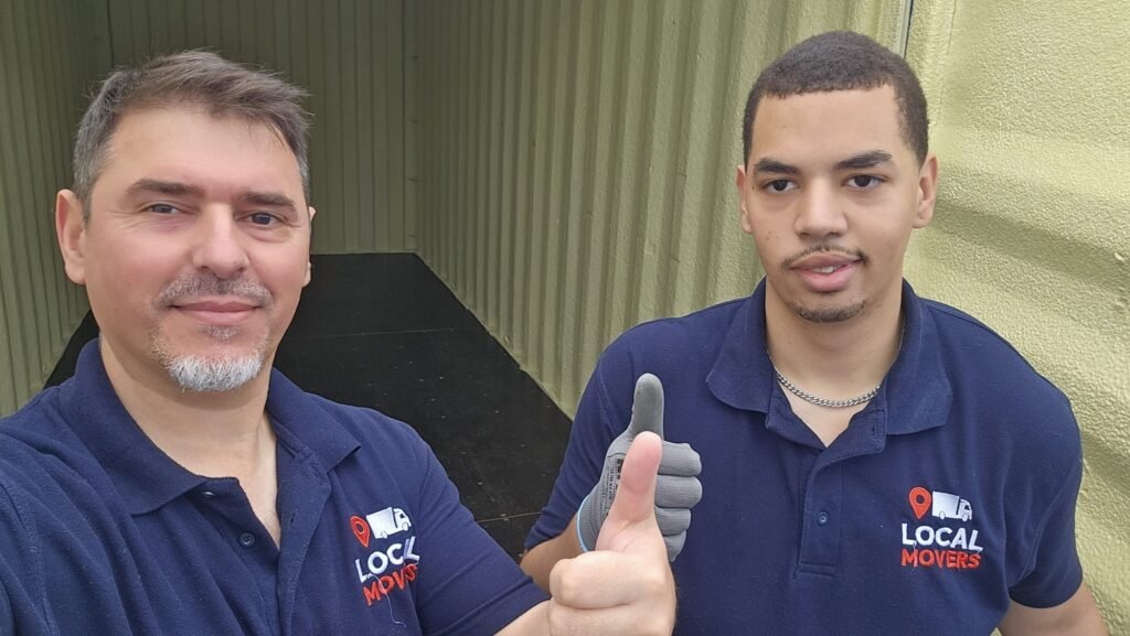 Two male movers in blue shirts with "Local Movers" logo give a thumbs up inside a moving container, ready for a move from Dublin to Sligo.