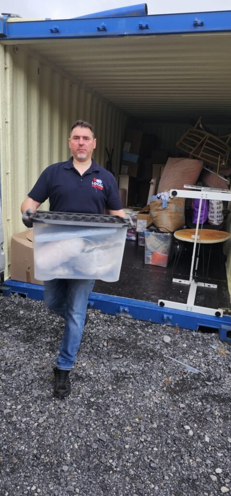 Man carrying a clear plastic bin filled with items into a shipping container, likely part of a move from Dublin to Sligo.
