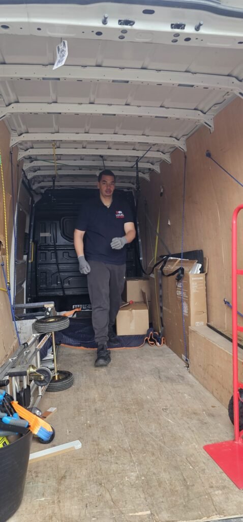A mover in a dark blue shirt and grey pants, wearing grey gloves, walks inside a moving van, preparing for a move from Dublin to Sligo. Boxes and moving equipment are visible.