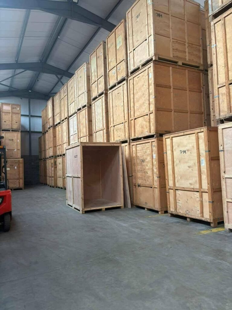 Rows of large wooden storage crates stacked high inside a warehouse, possibly used for moving from Dublin to Sligo. Some crates have numbers like '381' and '714' visible.