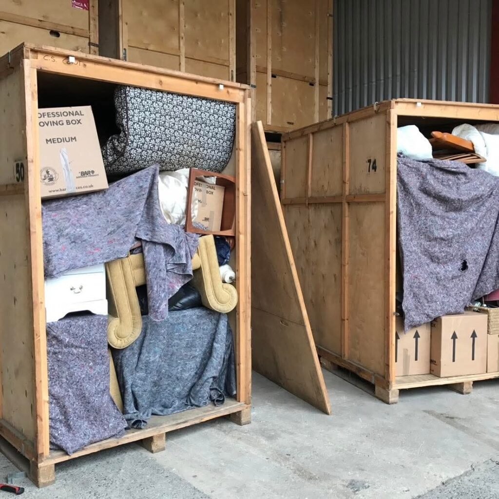 Two large wooden crates filled with household items, blankets, and boxes, ready for moving from Dublin to Sligo. One crate shows "PROFESSIONAL MOVING BOX" and "MEDIUM" text.
