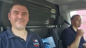 Two Local Movers employees in uniform, one smiling and the other giving a thumbs up, sit inside a moving van during a commercial relocation.