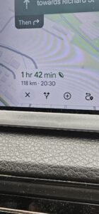Navigation app on a car dashboard shows a 1 hr 42 min, 118 km trip to Richard St, with a leaf icon indicating an eco-friendly route.