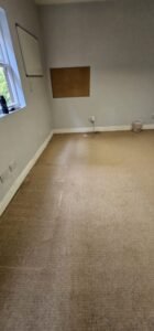 Empty office room with beige carpet, light gray walls, a window, and a corkboard, ready for commercial relocation.