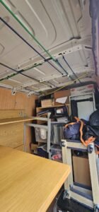 Interior view of a moving van packed with office supplies, furniture, and boxes, secured with colorful bungee cords and straps, ready for commercial relocation.