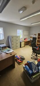 An empty office space with filing cabinets, desks, chairs, and scattered office supplies, suggesting a recent commercial relocation or office move.