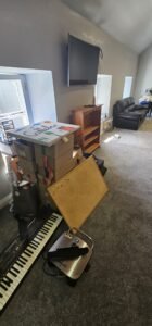 Boxes, a keyboard, and a corkboard are piled up in a room during a commercial relocation, showcasing the organized chaos of office movers.