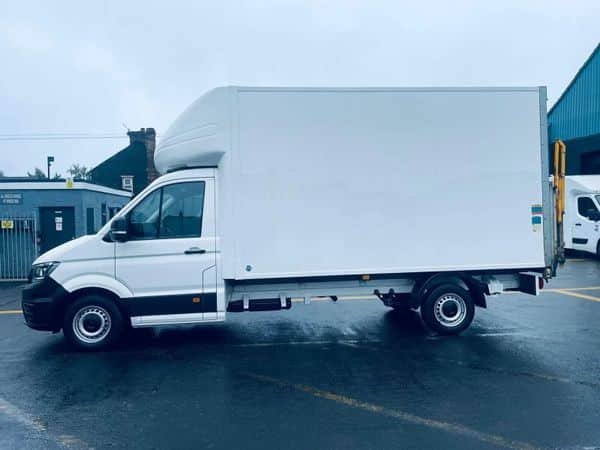 White box truck parked on a wet asphalt surface, ready for moving services. The truck features a large cargo box and a side door, with a building in the background.